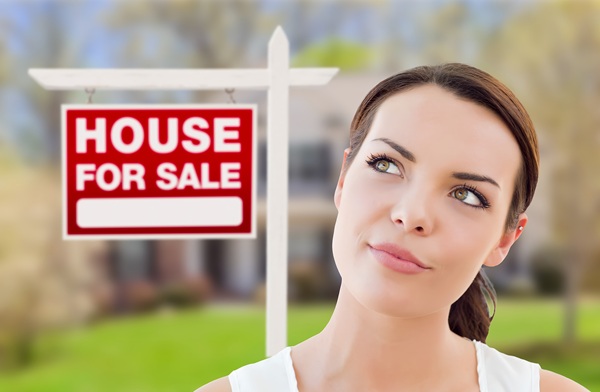 Woman considering selling her home with a For Sale sign, representing verified seller leads